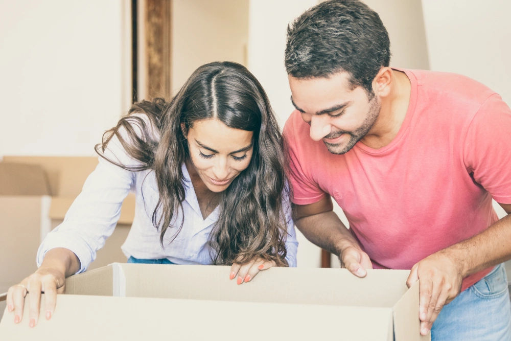 happy excited young latin couple opening carton box looking inside moving unpacking things